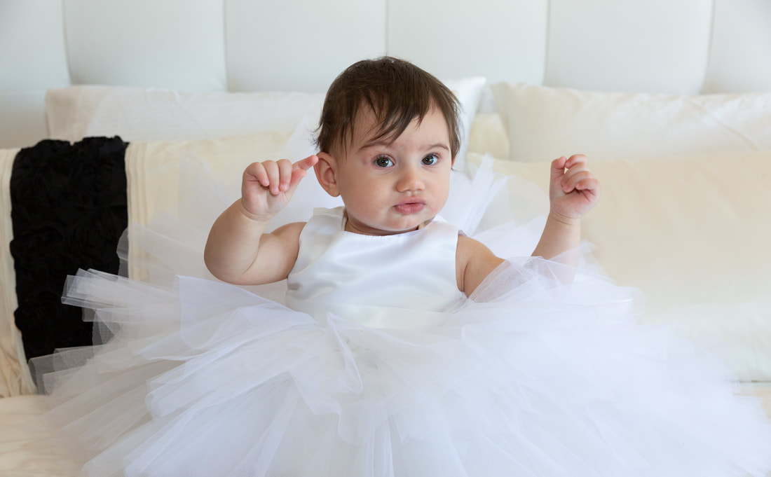 Amelia sitting on the bed at home in her beautiful christening gown.